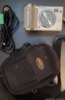 Front view of silver Fujifilm FinePix E510 camera, USB cord and black camera pouch