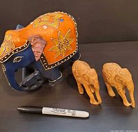 Painted blue/orange elephant with two natural wood elephants beside Sharpie for scale