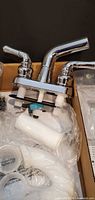 Chrome two-handle faucet atop white PVC parts in box
