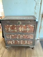 Front view showing decorative panels, two drawers, brass hasp, casters