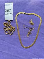 All five gold-tone necklaces displayed on purple fabric
