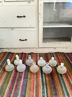 All nine milk glass hobnail perfume bottles displayed on rug