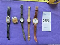 All five wristwatches laid out side by side on purple fabric