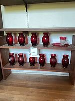 Shelf with 11 ruby red vases, pitcher on matching plate