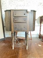 front view of wooden sewing cabinet with three drawers and drop-leaf sides