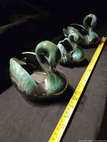 Top view of three drip-glazed swan figurines beside measuring tape