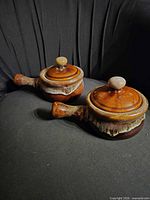 two lidded soup crocks on dark background