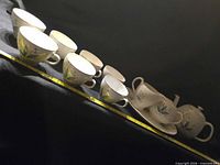 Row of eight teacups plus serving pieces on measurement tape
