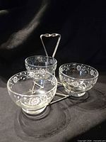 three etched glass bowls seated in metal caddy, lids removed