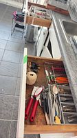 Both drawers open showing assorted utensils, flatware and tools