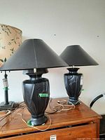 Two black ceramic lamps with black shades atop wooden surface