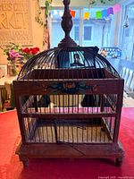 Front view of wooden birdcage showing domed wire top, floral panel and door