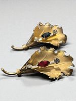 Front view of both gold gilt leaf brooches showing red and blue navette stones and clear accents