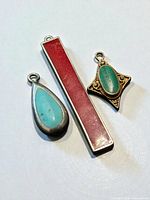 Front view of three pendants: turquoise teardrop in sterling, red enamel bar in sterling, malachite diamond in copper