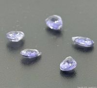 Five loose faceted tanzanite gemstones on dark background