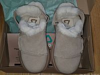 Top view of both slippers in box with tissue and branding visible