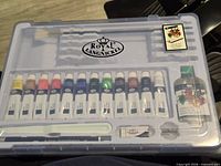 Closed case showing brand logo and visible contents through lid: paint tubes, linseed oil, tools