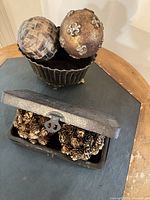 Bowl holding two decorative balls, box opened showing pinecone spheres