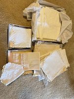 Overview of four groups of folded white and ivory linens in boxes and bags