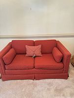 Front view of brick red loveseat with bolsters and throw pillow