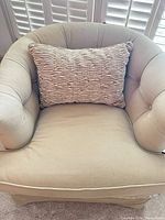 Front view of light beige skirted barrel armchair with pillow