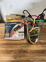 Retail package of CargoLoc 2-pack ratchet tie downs beside jar of bungee cords