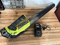 Full view of Ryobi cordless leaf blower with attached nozzle, charger and battery beside