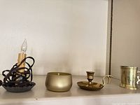 All four items on shelf: electric candle lamp, gold container candle, brass chamberstick, brass cup