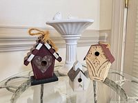 Group view of three wood birdhouses and white ceramic pedestal dish