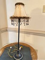 Full view of lamp showing base, stem, shade with fringe and bead tassels