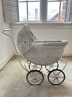 Side view of white wicker doll pram showing wheels, handle and hood