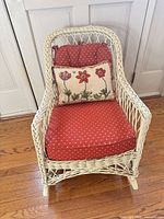 Front view of painted wicker rocking chair with red cushions and floral pillow