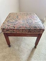 Stool standing upright showing tapestry seat and wood frame on carpet