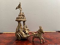 Left-front view of entire brass chariot sculpture showing figures, canopy, horse and wheels