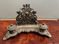 Front view of entire ornate metal desk set showing two lidded inkwells and decorative letter rack
