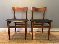 Front view of both teak/beech chairs showing curved backs and black seats