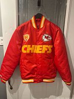 Front view of red Mitchell & Ness Chiefs bomber jacket hanging