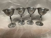 Four small silver-tone metal stemmed goblets side by side