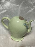 Front three-quarter view showing peach form, spout with leaf decoration and handle