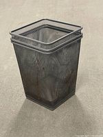 Angled view of stacked metal mesh bin showing rim and mesh construction, surface wear