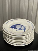 Stack of eight white ceramic plates with blue koi design, front view