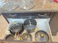 Drawer containing six nonstick pots and pans with labels; two glass lids placed on countertop
