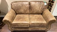 Front view of brown faux leather Ashley loveseat showing cushions, rolled arms, nailhead trim