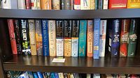 Full shelf showing twelve hardback books by Ludlum, Clancy, Brown, Follett, Bryson, Larsson