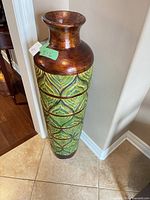 Full view of tall green and bronze vase against wall