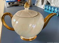 Full view of teapot showing ivory body and gold handle, spout, finial and foot
