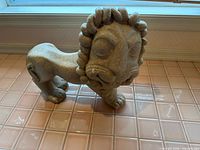 Front and side view of full-body concrete lion statue on tiled surface