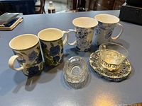 Group view of all four mugs, BMF teacup in holder on metal saucer, pressed glass salt cellar