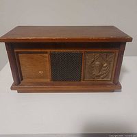 Front view showing wood case, three front panels including speaker grille and carved decoration