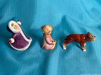 Group shot of the three Goebel porcelain figurines: hooded child, kneeling girl, bulldog
